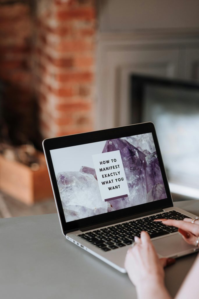 Image of someone typing on a MacBook that has an image of the phrase, "How to Manifest Exactly What You Want" on a card on the screen.