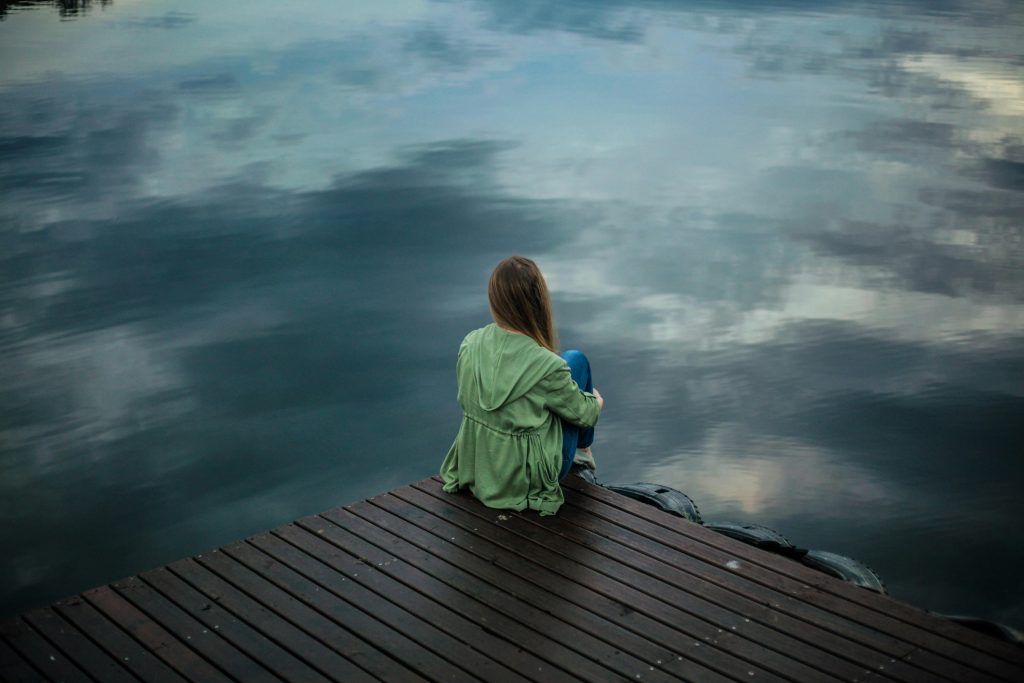 Loan person with their back to the camera looking into a grey lake on a cloudy day.